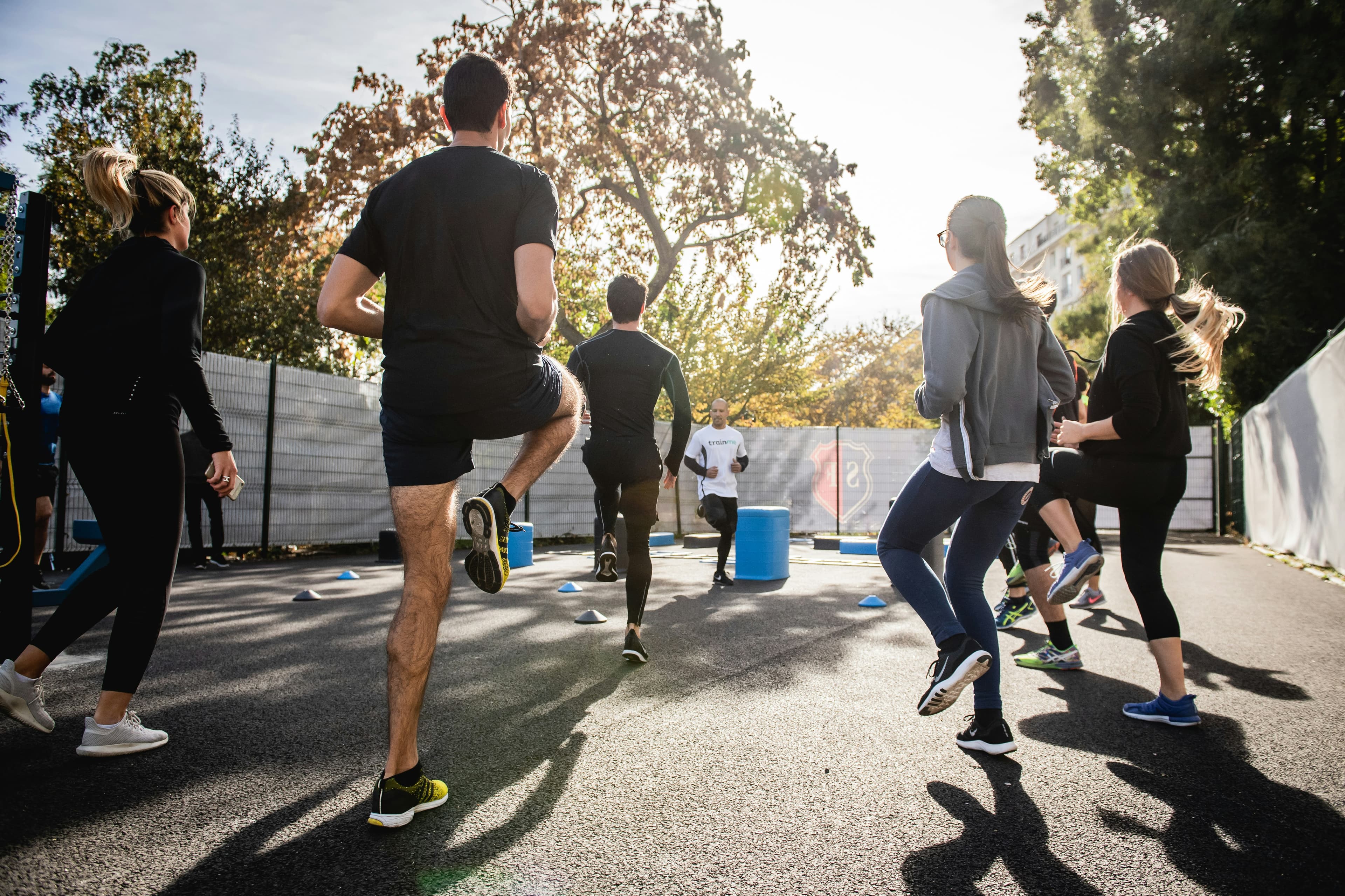 Group of runners jogging together down a sunlit tree-lined street, seen from behind